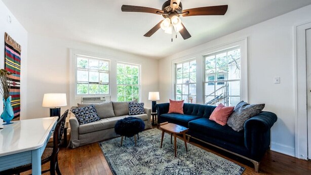 A living room with a sofa, two chairs, a coffee table, and a rug. There are two windows with views of greenery outside. - The Charmer, Super Close to UT + Downtown (Austin)