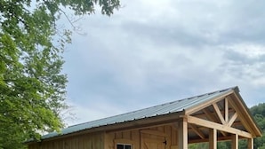 A wooden cabin with a porch and a covered area, surrounded by greenery. - Enjoy nature in a cabin getaway, wildflowers, lush fields and maple woods trails (Cambridge)