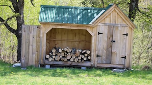 A wooden shed with a green roof, used for storing firewood. - Enjoy nature in a cabin getaway, wildflowers, lush fields and maple woods trails (Cambridge)