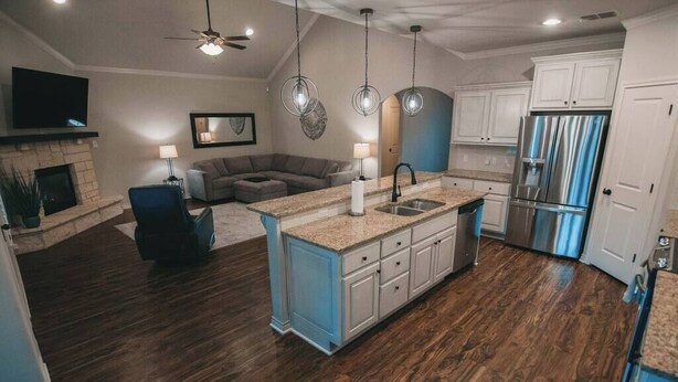 A modern kitchen with a central island, built-in appliances, and a cozy living area with a fireplace and seating. - Spark Getaways: The Ricardo (Lubbock)