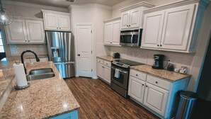 A kitchen with white cabinets, stainless steel appliances, granite countertops, and a wooden floor. - Spark Getaways: The Ricardo (Lubbock)