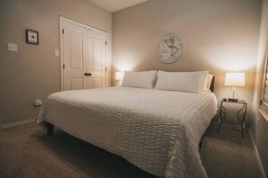Ein Schlafzimmer mit einem großen Bett, zwei Nachttischlampen, einer Tür und einer Wanduhr.