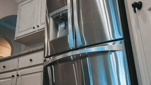 A stainless steel refrigerator in a kitchen with white cabinetry and a wooden floor. - Spark Getaways: The Ricardo (Lubbock)
