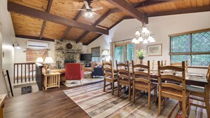 Un vaste espace dédié à la salle à manger, avec des chaises et une table en bois, une cheminée en pierre et une grande fenêtre donnant sur un paysage verdoyant.