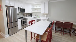 A modern kitchen with white cabinetry, stainless steel appliances, a white marble countertop, and red chairs. - 👣 Come get your toes in the sand Call today to book your Vacation! (Gulf Shores)