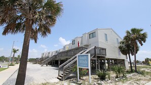 A building with a sign reading "South Winds to W. 2nd St." with a wooden staircase leading to the entrance. - 👣 Come get your toes in the sand Call today to book your Vacation! (Gulf Shores)