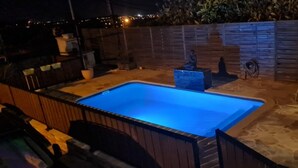 Una piscina rectangular con iluminación azul en su interior, rodeada por un patio de piedra y una terraza de madera.