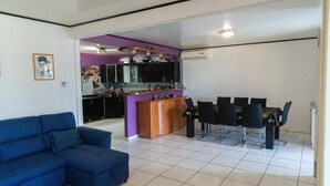 Una sala de estar moderna con un sofá azul, una zona de comedor con mesa y sillas, y una cocina con armarios morados y una isla central.