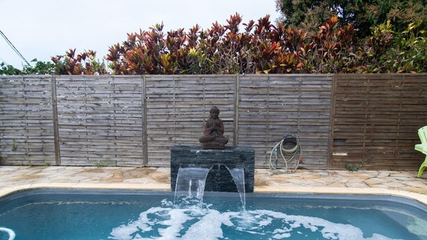 Una piscina con cascada, una estatua de Buda y un cerramiento de madera con follaje.