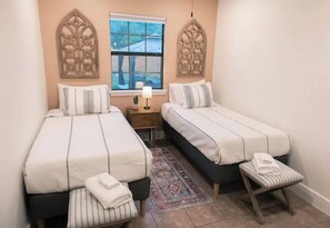 Ein Schlafzimmer mit zwei Betten, einem Nachttisch, einem Fenster und einer Wanddekoration.