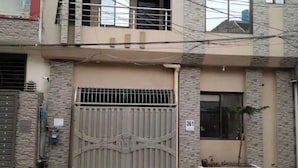 A two-story building with a gated entrance, a balcony on the upper floor, and a small plant in the front yard.