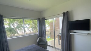 A hotel room with a large bed, a flat-screen TV mounted on the wall, and a view of the outdoors through the windows. - NEW OCEAN FRONT CONDO 2BR 2BATH full amenities (Bejuco)