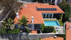 A residential property with a swimming pool, solar panels, and a well-maintained garden. - Casa Roc Madeira | 5 Bedrooms | Ocean and City Views, Private Heated Pool (Funchal)