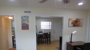 Une pièce spacieuse dotée de planchers en bois, d’un coin repas avec des chaises et une table, d’un bureau avec un ordinateur et une lampe, et d’œuvres d’art accrochées aux murs.