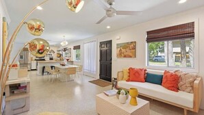 A modern living room with a sofa, coffee table, and a dining area with chairs. - Coligny Retro Beach House Ocean access, Pool, Grill, Kids Room! (Hilton Head Island)