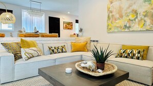 A modern living room with a sectional sofa, a coffee table, and a large abstract painting. - Coligny Retro Beach House Ocean access, Pool, Grill, Kids Room! (Hilton Head Island)