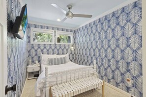 A bedroom with a bed, a bench, a ceiling fan, and a window.