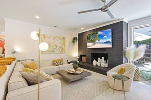 A modern living room with a fireplace, a large TV, and a ceiling fan.
