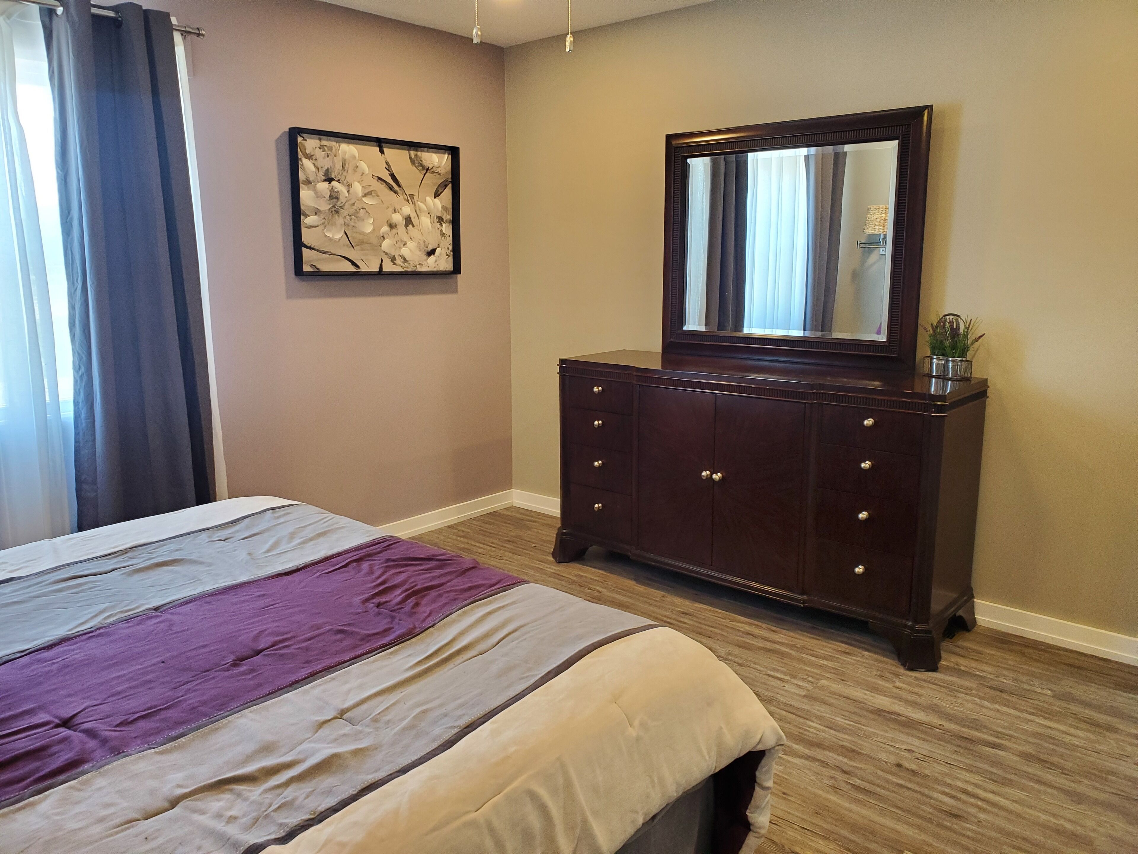 Een slaapkamer met een bed, een dressoir, een spiegel en een schilderij aan de muur.