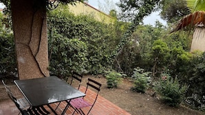 An outdoor patio with a table and chairs, surrounded by dense greenery and a tree. - House in Les Issambres 10 minutes walk from the beach (LES ISSAMBRES)