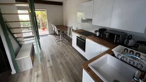 A modern kitchen with white cabinets, a wooden countertop, and a built-in oven. There is a dining area with a table and chairs, and a staircase leading to an outdoor area. - House in Les Issambres 10 minutes walk from the beach (LES ISSAMBRES)