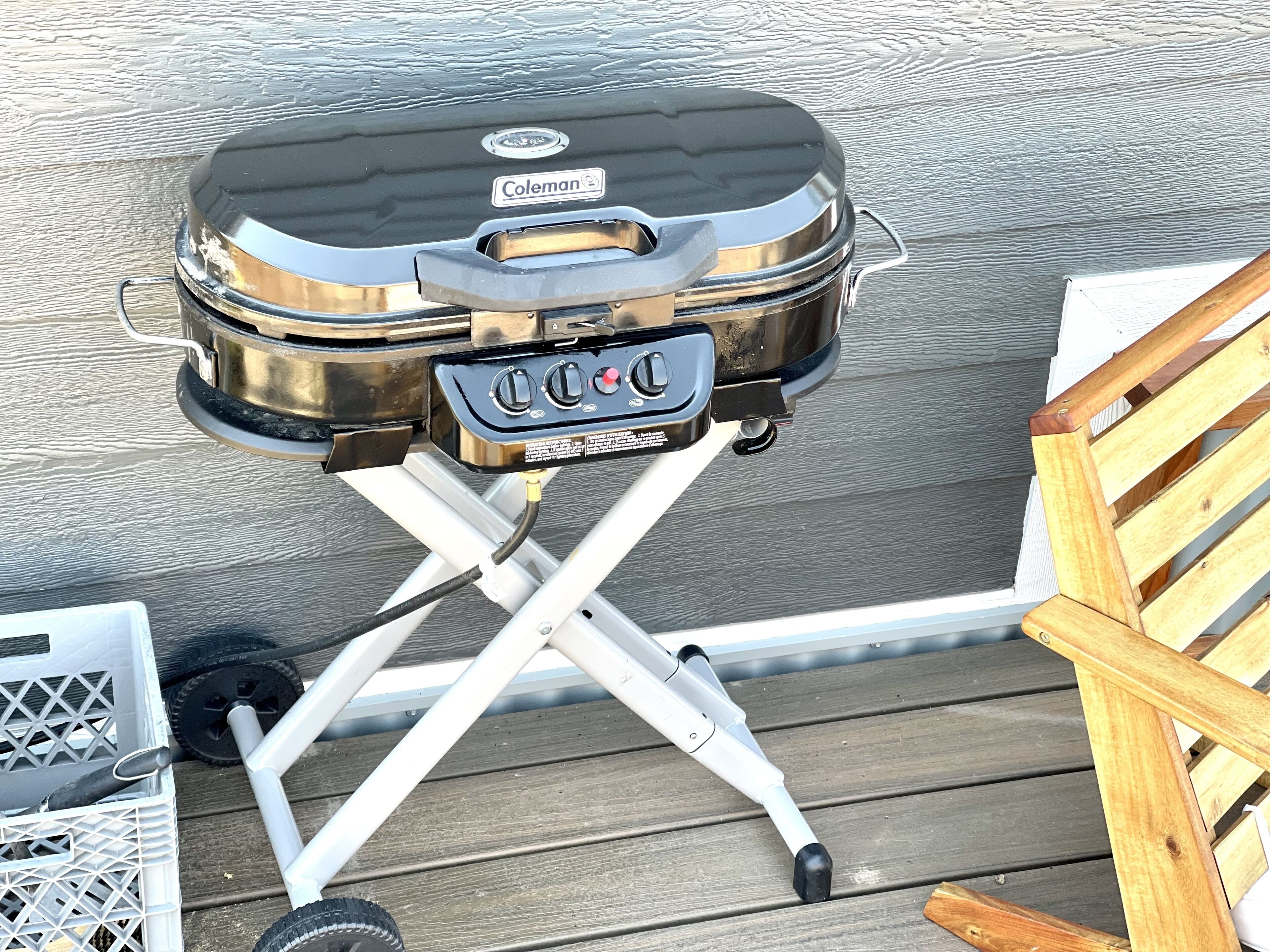 A Coleman portable grill on a white metal stand with wheels, placed on a wooden deck.