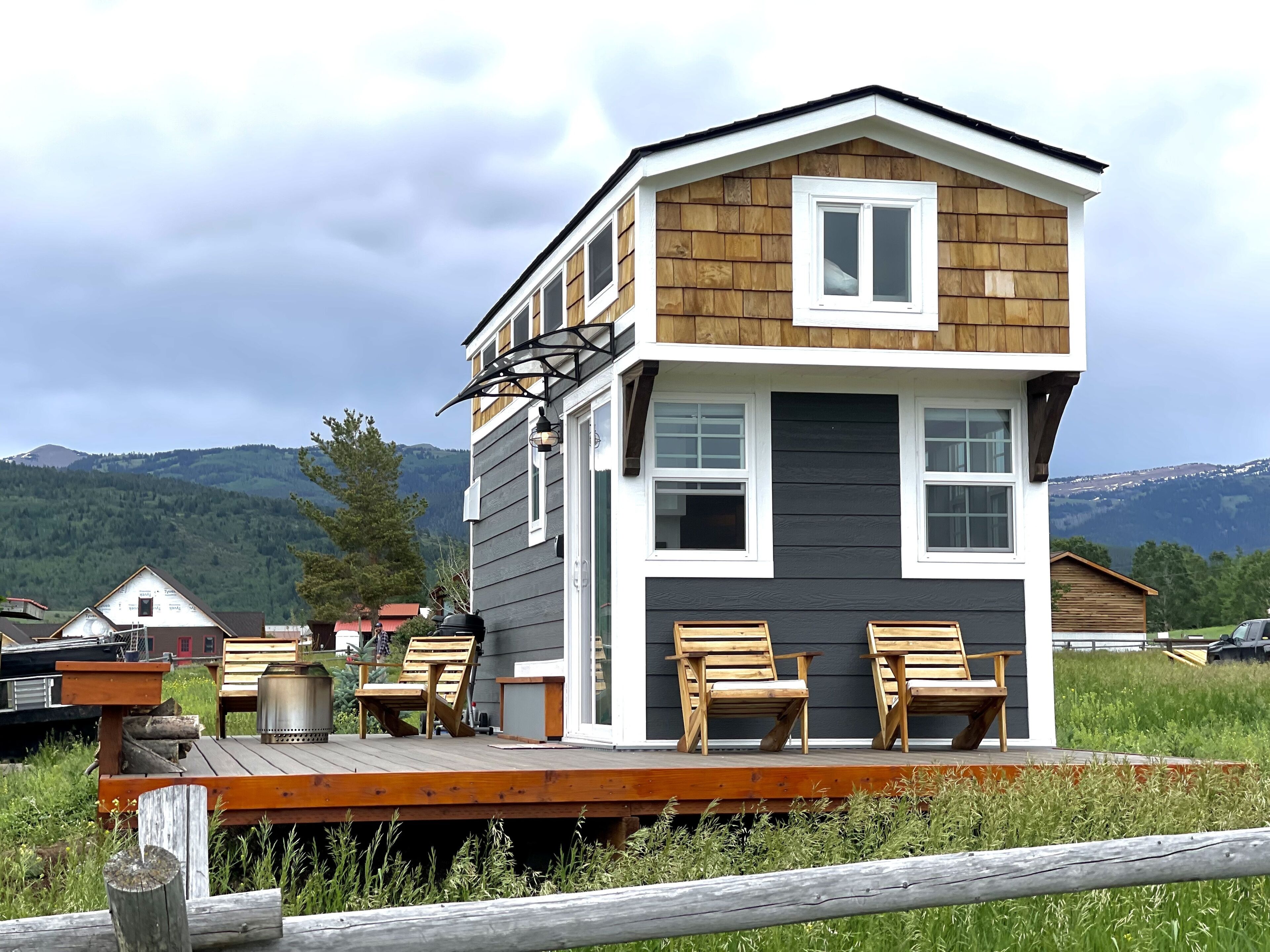 Een huis met twee verdiepingen, een terras, houten stoelen en een lantaarn.