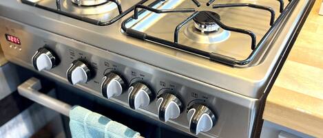 Une cuisinière à gaz en acier inoxydable, dotée de quatre brûleurs et d’un panneau de commande avec plusieurs boutons.