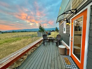 A deck with a table and chairs, overlooking a rural landscape with mountains in the distance. - Big View Tiny House, a luxury tiny house experience! (Victor)