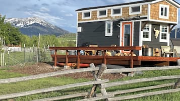 Una baita a due piani con veranda, circondata da una recinzione di legno, con montagne sullo sfondo.