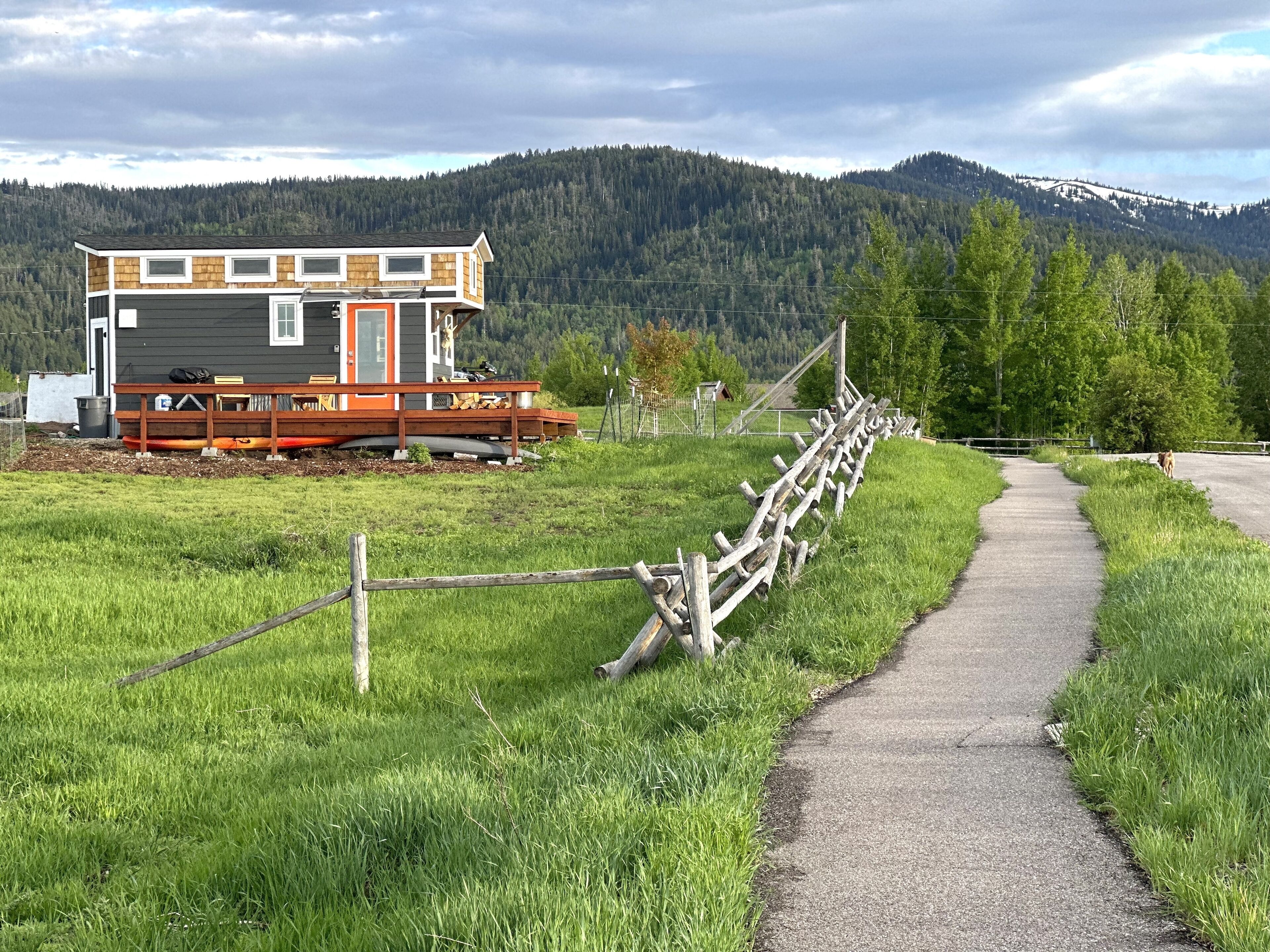 A cabin with a deck, surrounded by a wooden fence and a path leading to it.