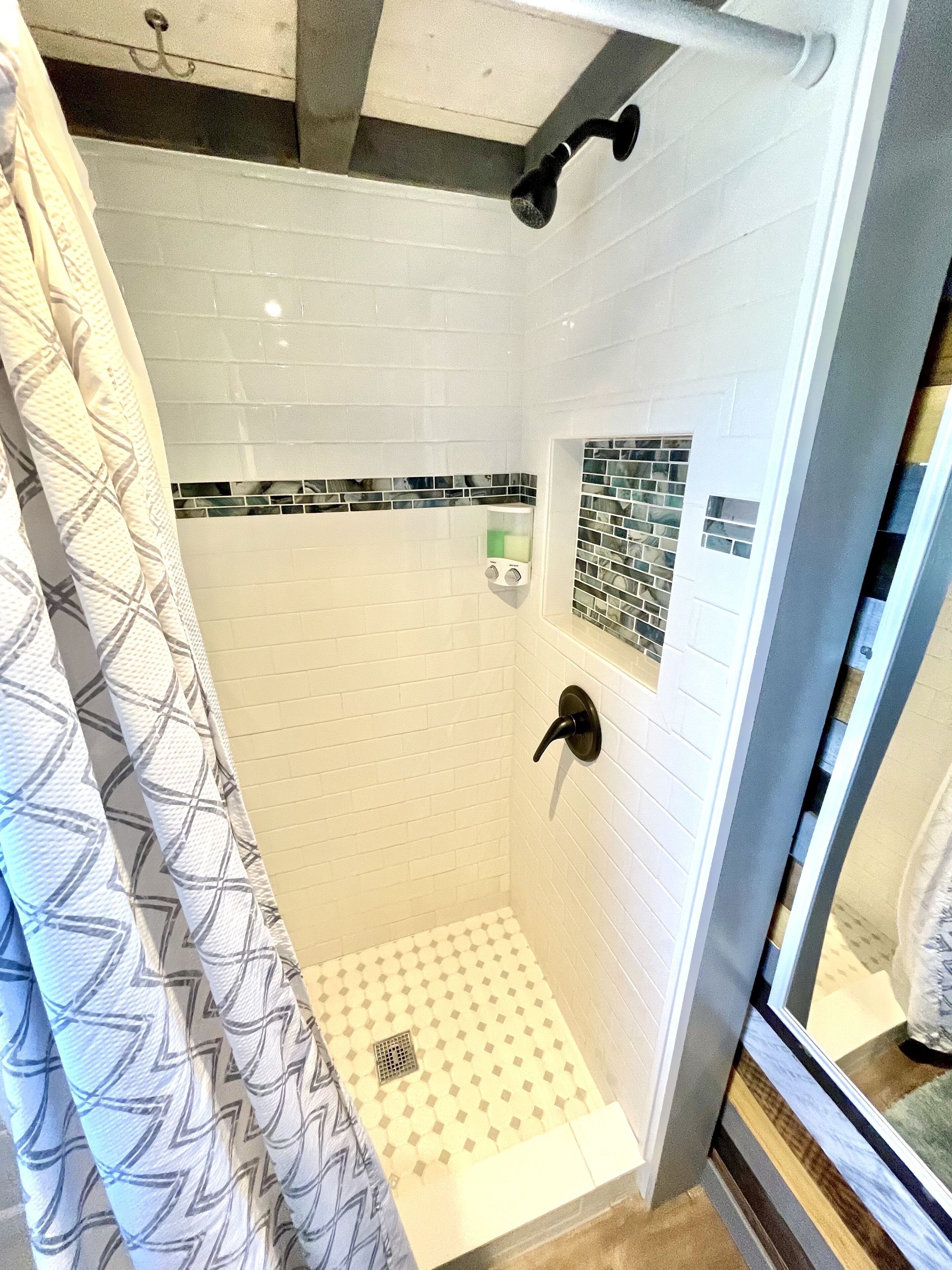 Ducha con azulejos blancos, puerta de vidrio y cortina estampada.