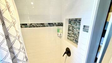 Ducha con azulejos blancos, puerta de vidrio y cortina estampada.