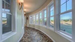 A curved hallway with stone flooring, large windows, and wall-mounted lighting. - Enumclaw Estate, Scenic Views! Sleeps12,HotTub,Sauna, 1hr frm Rainier & Crystal (Enumclaw)