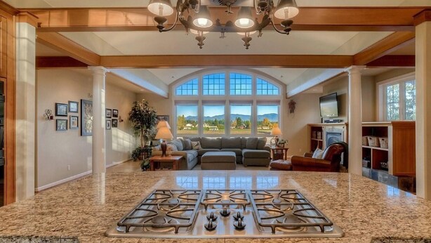 A spacious kitchen with a central island, large windows offering a view of the outdoors, and a cozy seating area with a fireplace. - Enumclaw Estate, Scenic Views! Sleeps12,HotTub,Sauna, 1hr frm Rainier & Crystal (Enumclaw)
