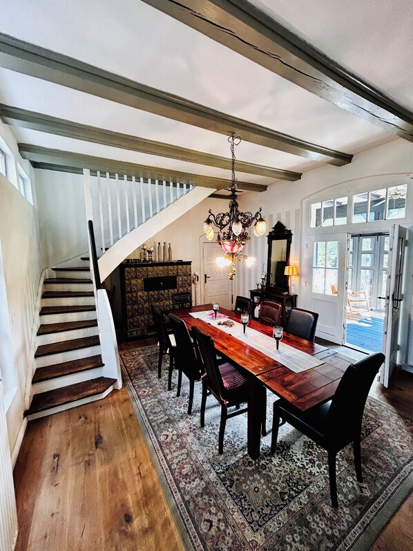 A dining area with a wooden table, chairs, a chandelier, and a staircase.