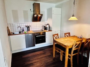 A compact kitchen with a dishwasher, stove, and a dining table with chairs.