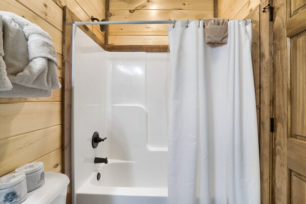 A wooden cabin bathroom with a white bathtub, a towel hanging on the wall, and a toilet with toilet paper.