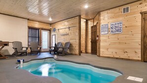 An indoor pool area with wooden walls, a pool with a blue edge, and two Adirondack chairs.