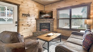 A cozy living room with a stone fireplace, wooden walls, and a 'Welcome' sign.