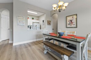 Een eethoek met een houten bank, een glazen tafel en rode placemats.