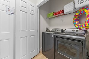 A laundry room with two washing machines and a dryer, a white door, and a shelf with folded towels and a colorful ring.
