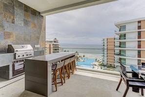 A modern kitchen with a grill, bar stools, and a view of a pool and buildings.