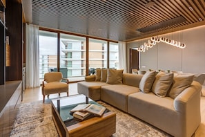 A modern living room with a sectional sofa, a glass coffee table, and a view of a residential building through large windows.