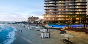 A beachfront hotel with a swimming pool, lounge chairs, and a view of the ocean.