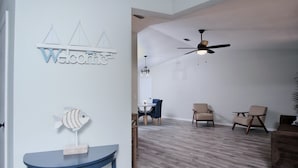 Un salon moderne avec un plancher en bois, un ventilateur de plafond et un coin repas avec des chaises bleues.