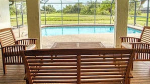Une terrasse extérieure avec un banc en bois, une table et une vue sur une piscine et la verdure.