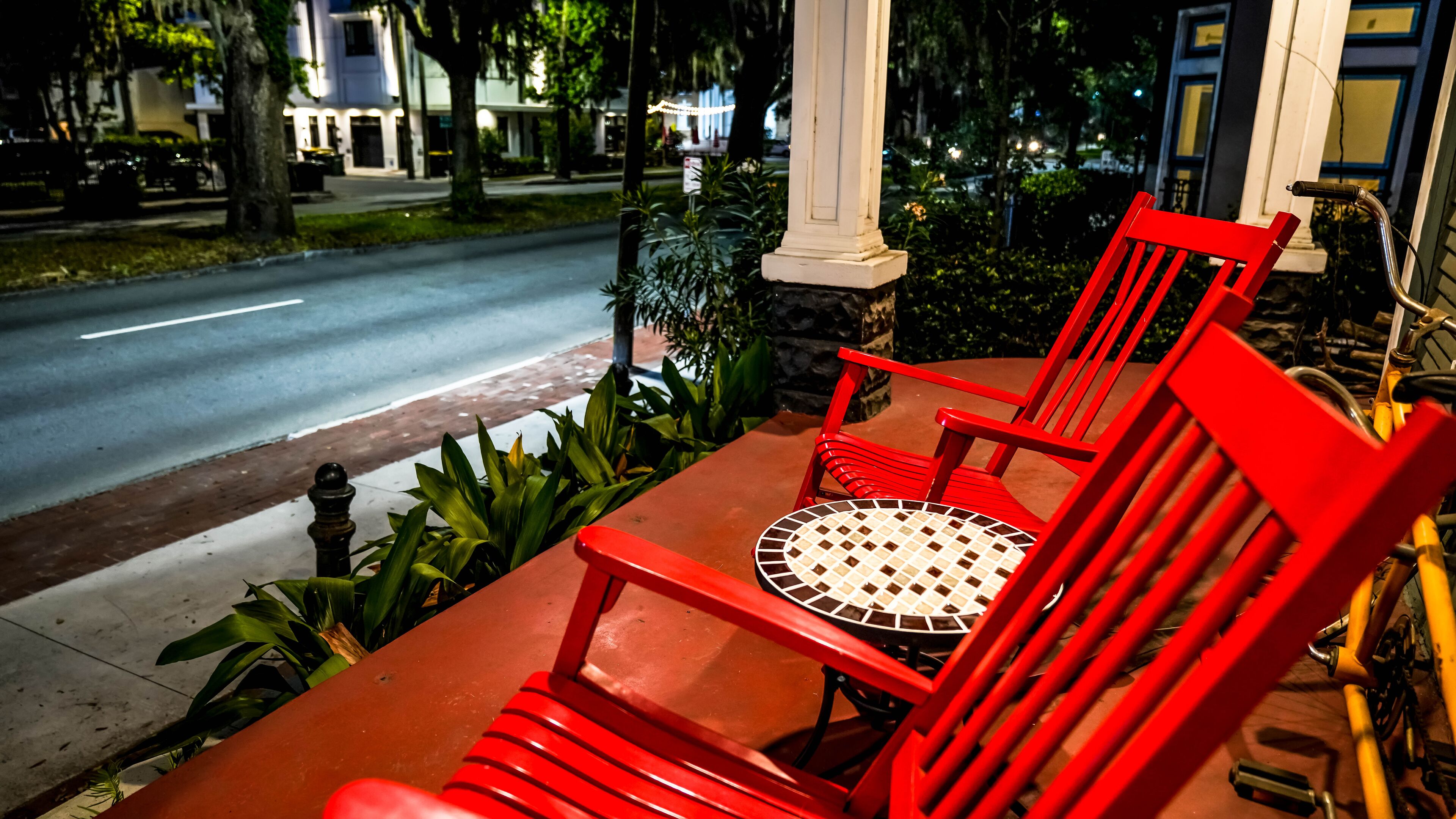Una silla roja y una mesa en un porche con vista a la calle.