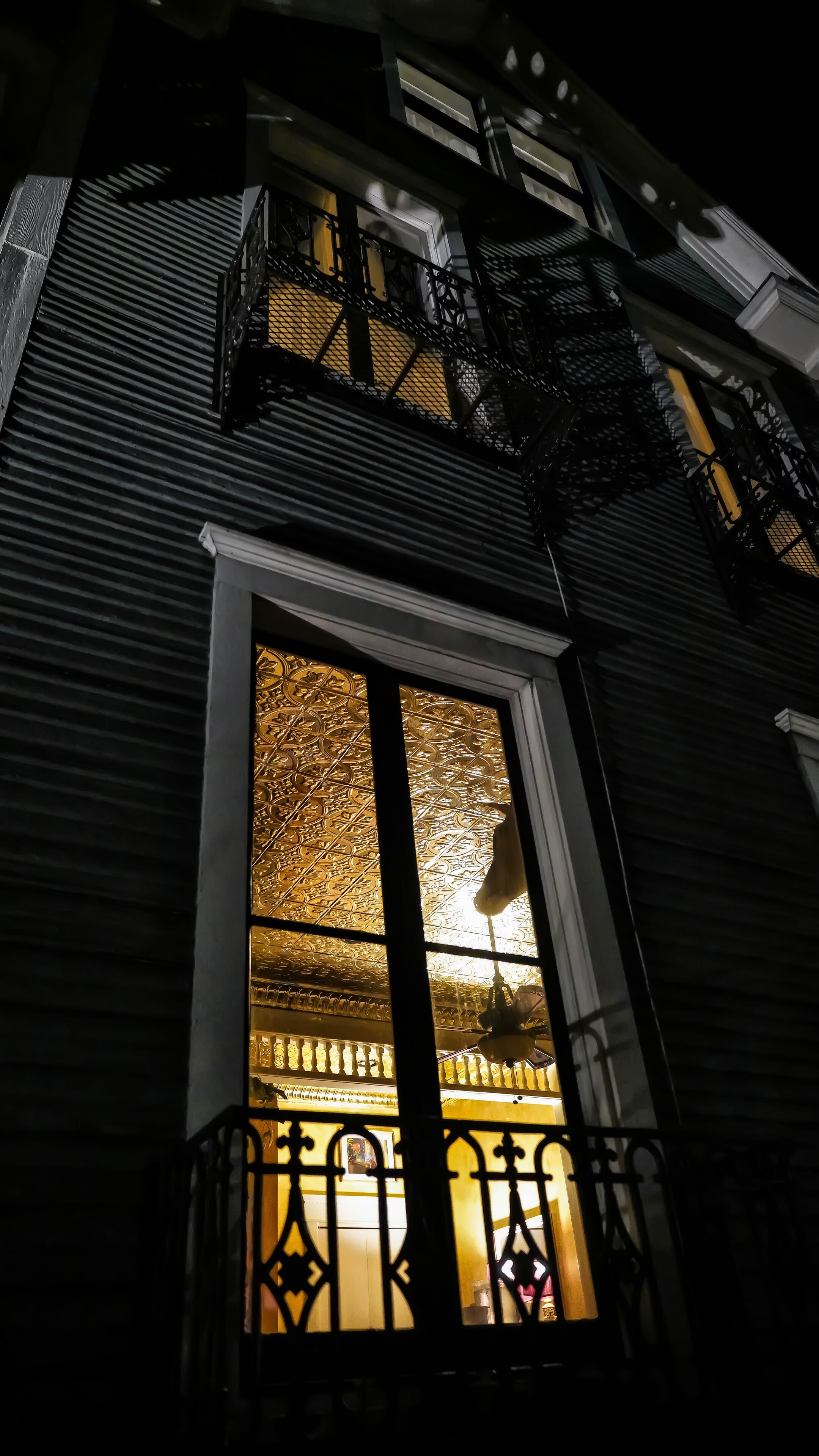 A building with a large window featuring intricate metalwork and a balcony with a black railing.