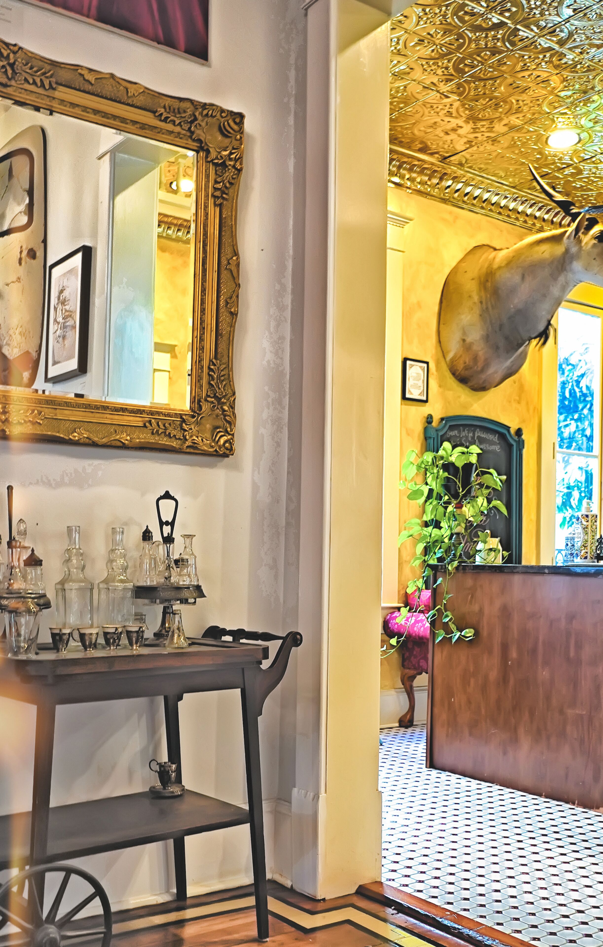 A vintage-style room with a wooden table, a large ornate mirror, and a decorative ceiling.